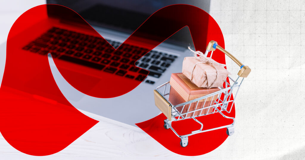 A tiny shopping cart loaded with boxes sits by an open laptop